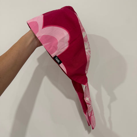 Pink and red cherry blossom floral patterned headscarf held by a hand on a light background
